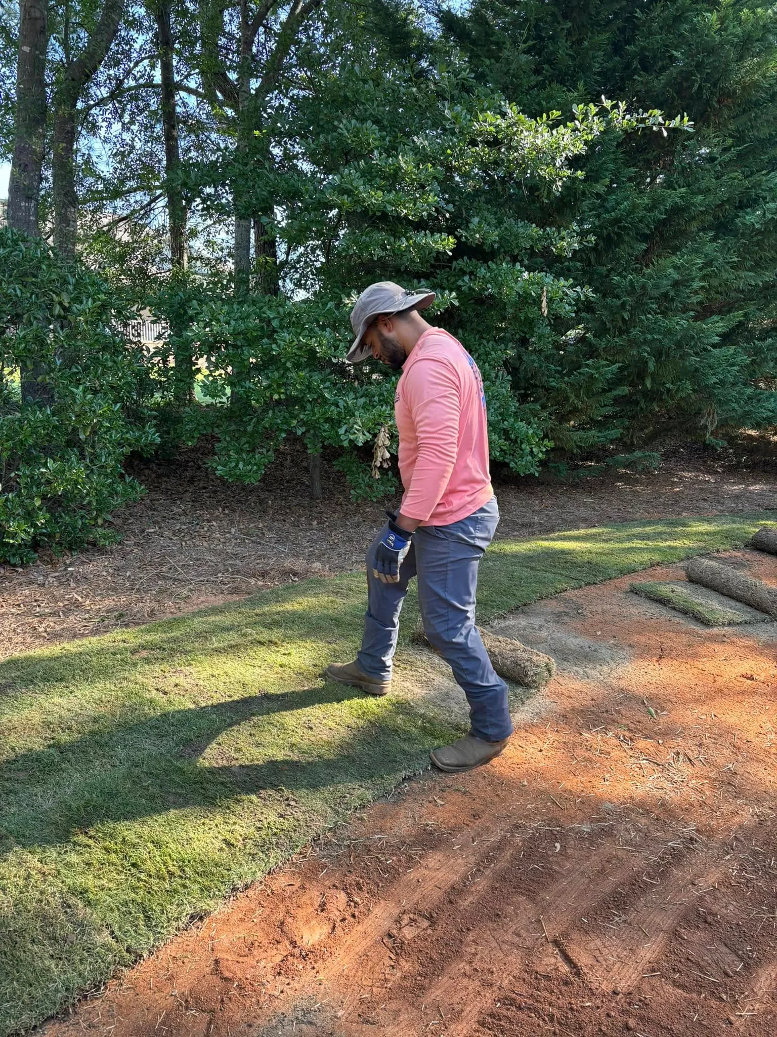 Worker laying sod rolls red clay backyard
